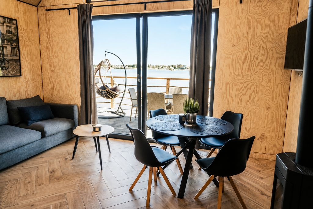 Nowoczesny salon z jadalnią, tarasem nad wodą, szarą sofą i czarnym stołem z krzesłami